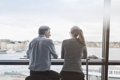 Rear view of business people sitting at counter by window in office