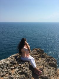 Woman sitting on rock looking at sea against sky