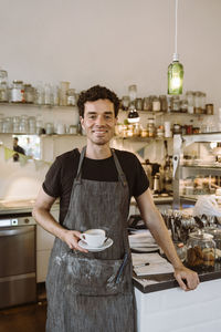 Smiling male owner holding coffee cup standing in cafe