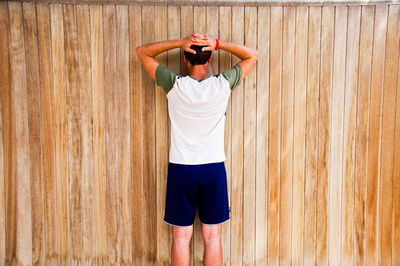 Rear view of man standing against wooden wall