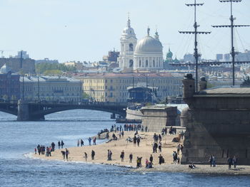 People at beach in city against buildings and sky