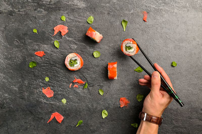 Cropped image of man holding sushi with chopsticks on stone tray