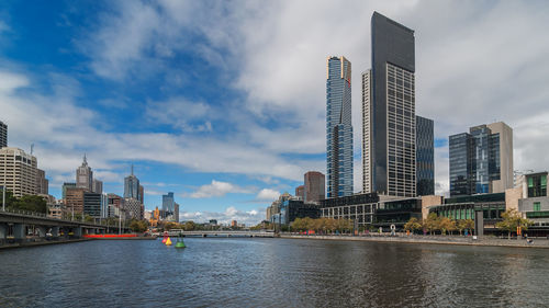 Modern buildings by river against sky in city