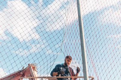 Low angle view of man looking through chainlink fence