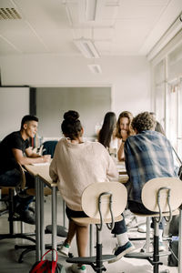 Rear view of teenage students studying by table in classroom