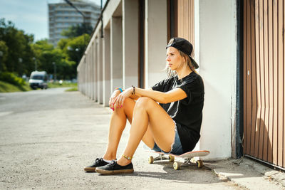 Side view of woman with skateboard sitting in city