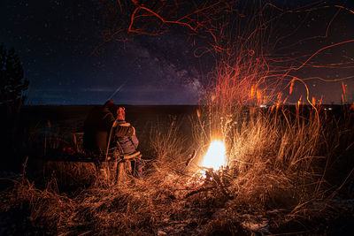 People sitting by bonfire against sky at night
