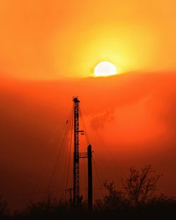 Silhouette oil pump against orange sky during sunset