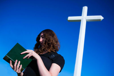 Low angle view of woman reading bible while standing cross