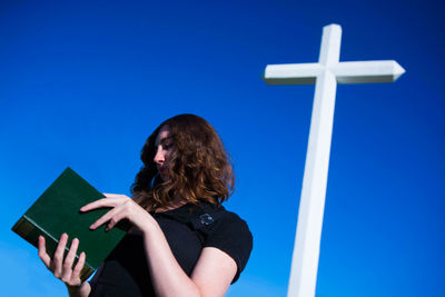 Low angle view of woman reading book against blue sky