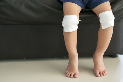 Low section of boy sitting on sofa with bandage on knees