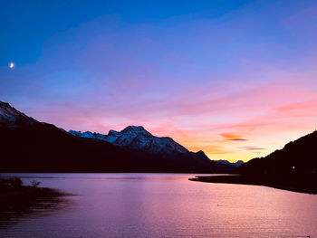 Scenic view of lake by silhouette mountains against sky during sunset