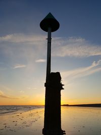 Silhouette wooden post on beach against sky during sunset