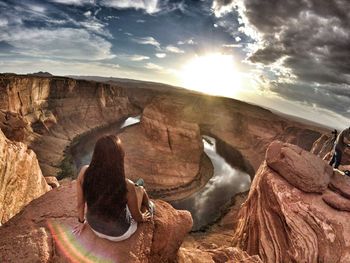 Rear view of woman sitting on cliff against horseshoe bend