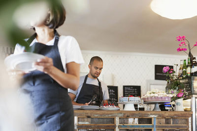 Woman holding plate and walking against male colleague working at cafe counter