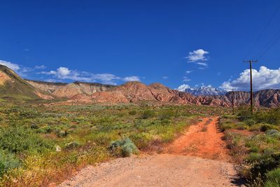 Dirt road amidst landscape against blue sky