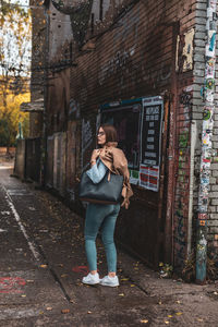 Full length portrait of woman standing on footpath against building in city