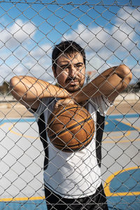 Portrait of young man seen through chainlink fence