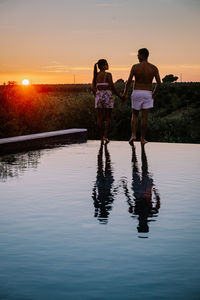 Rear view of couple standing by pool against sky during sunset