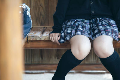 Midsection of woman sitting on bench during winter