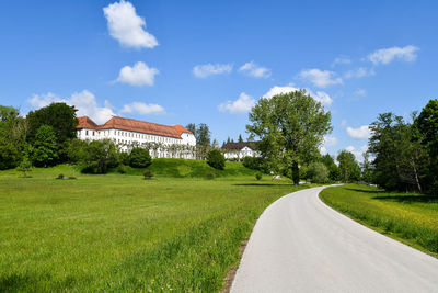 Road amidst field and trees against sky