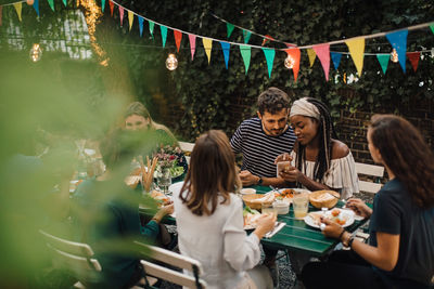 Young male and female friends with food at table during dinner party in backyard