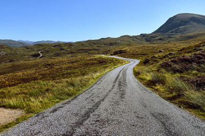 Road leading towards mountains against clear sky