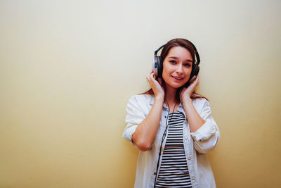 Portrait of young woman listening to music against wall