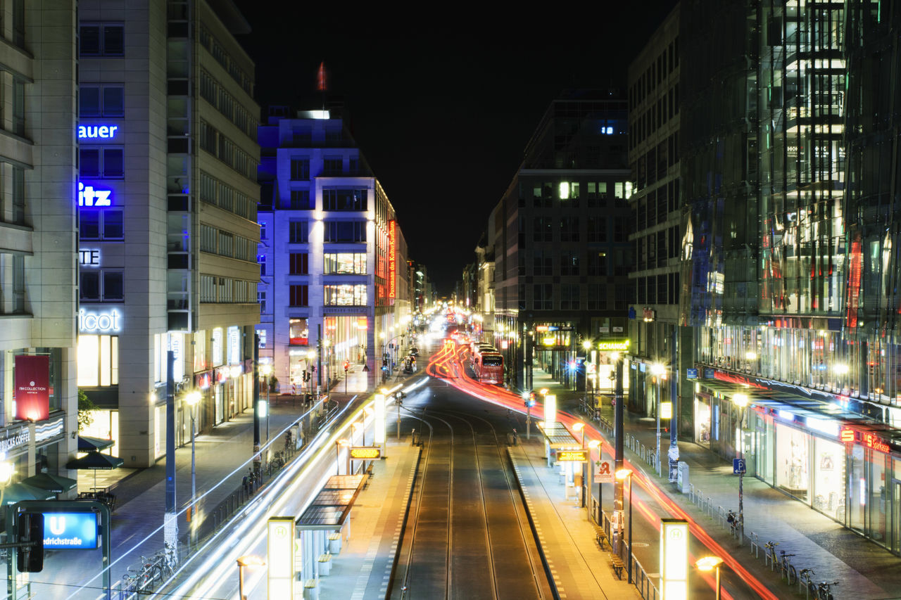 LIGHT TRAILS ON ROAD ALONG ILLUMINATED BUILDINGS