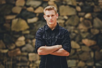 Portrait of young man with arms crossed standing against wall