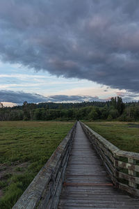 Wooden boardwalk on field against sky