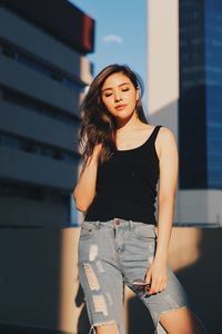 Young woman wearing torn jeans looking away standing against building on terrace 