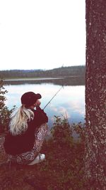 Woman sitting by lake against sky