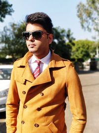 Young man wearing long coat on road during sunny day