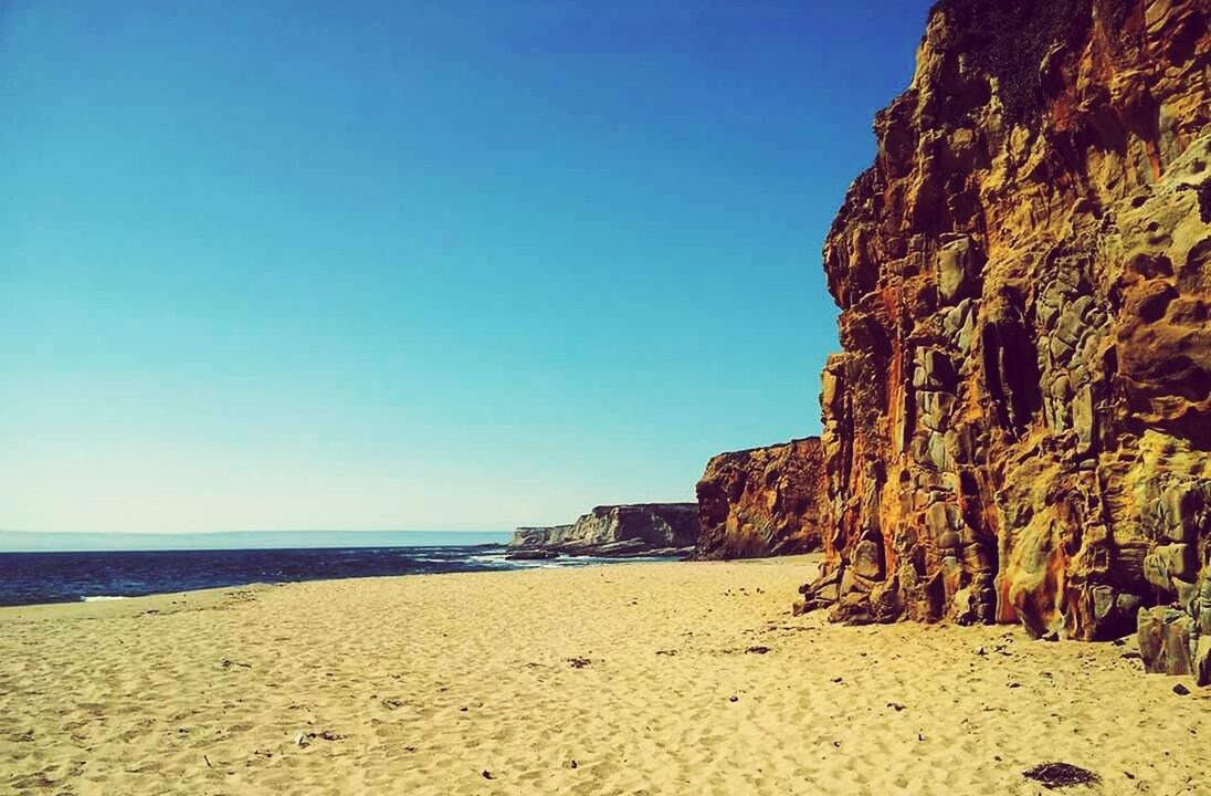 sea, clear sky, beach, sand, tranquil scene, tranquility, rock formation, scenics, beauty in nature, blue, copy space, water, shore, horizon over water, nature, cliff, rock - object, idyllic, coastline, sunlight