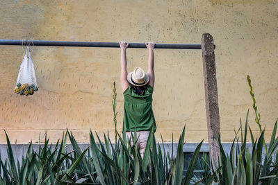 Rear view of woman hanging against yellow wall