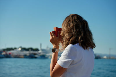 Young woman using mobile phone while standing against sea