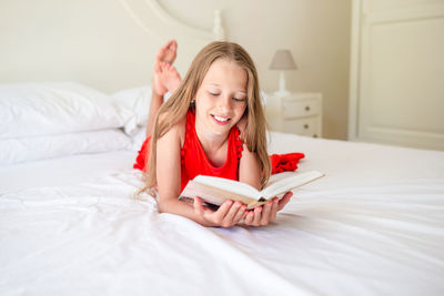 Full length of girl reading book lying on bed at home