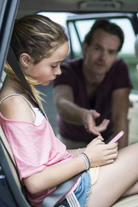 Daughter ignoring father while using mobile phone in car