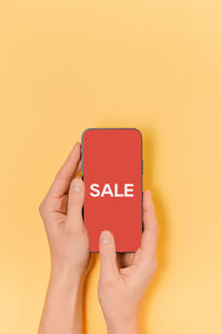 Cropped hands of woman using smart phone against yellow background