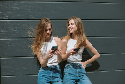 Young woman using mobile phone while standing on wall