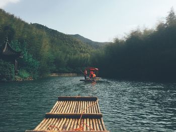 Wooden raft on river with people in boat against mountain