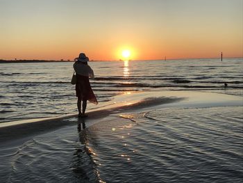 Rear view of man standing on beach during sunset