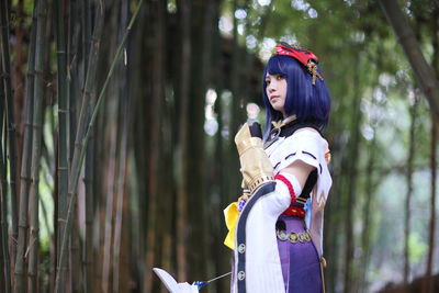 Side view of young woman standing against trees