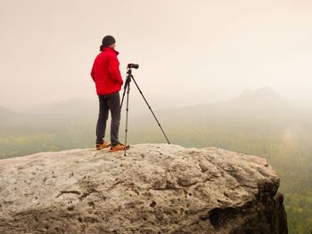 Photographer think about picture on peak in mountains. photograph above valley hidden in heavy mist. 