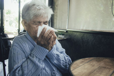 Old person coughing covering mouth with a tissue on a house interior. she has flu, allergy symptoms.