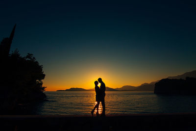 Silhouette people standing on sea against sky during sunset