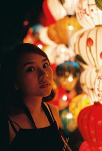 Close-up portrait of young woman by illuminated lanterns