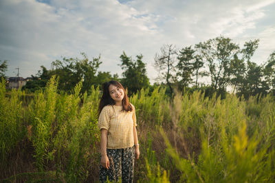 Portrait of smiling young woman standing on land against sky