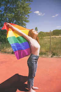 Full length of young woman holding rainbow flag on sunny day
